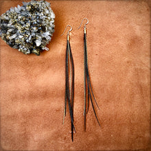 Load image into Gallery viewer, Black coque feather and gold chains hang from a gold earwire next to a geode rock