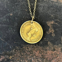 Load image into Gallery viewer, Gold coin pendant with zodiac design on a chain against a dark stone background