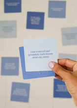 Load image into Gallery viewer, Hand holding a blue card with text against a wall with more blue cards.