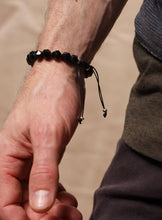 Load image into Gallery viewer, Close-up of a wrist wearing a black beaded bracelet on a blurred background