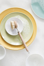 Load image into Gallery viewer, Dishwashing brush on a plate with soap suds, surrounded by other dishes on a light surface.