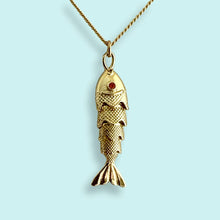 Load image into Gallery viewer, Gold fish-shaped pendant with a red gemstone on a light blue background