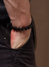 Load image into Gallery viewer, Close-up of a wrist wearing a black beaded bracelet on a brown background
