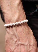 Load image into Gallery viewer, Close-up of a wrist wearing a white beaded bracelet against a blurred background