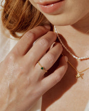 Load image into Gallery viewer, Close-up of a hand wearing a gold ring with a green gemstone, touching a pearl necklace.