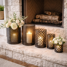 Load image into Gallery viewer, Decorative candles in metal holders with flowers on a stone fireplace.