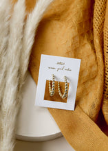 Load image into Gallery viewer, Gold hoop earrings on a branded card with a textured mustard yellow fabric background