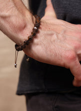 Load image into Gallery viewer, A close-up of a person's wrist wearing a dark brown faceted gemstone beaded bracelet with a small silver geometric accent and a sliding cord closure.