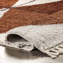 Load image into Gallery viewer, Close-up of a brown and white checkered rug with tassels on a wooden floor.