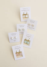 Load image into Gallery viewer, Set of earrings on display with their packaging on a beige background