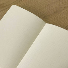 Load image into Gallery viewer, Open notebook with dot grid on cream pages on a wooden surface