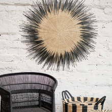 Load image into Gallery viewer, One Usiku Woven Wall Art pieces with a natural enter and black indigo edging displayed on a wall with a chair and side basket.