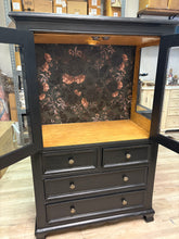 Load image into Gallery viewer, Black cabinet with glass shelf and drawers on a wooden floor
