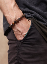 Load image into Gallery viewer, A close-up of a person's hand in a pocket wearing a beaded bracelet made of brown, black, and orange stones.