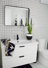 Load image into Gallery viewer, Bathroom with white vanity, mirror, and plant on a tiled wall.