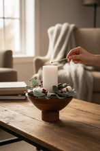 Load image into Gallery viewer, Person lighting a candle in a decorative wood bowl on a wooden table in a cozy living room.