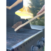 Load image into Gallery viewer, Person using a grill brush to clean a barbecue grill outdoors.