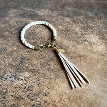 Load image into Gallery viewer, White braided bracelet with a tassel on a textured brown surface