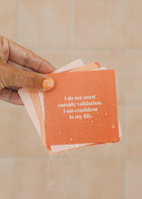 Load image into Gallery viewer, Hand holding a stack of orange cards with motivational text against a beige tiled wall.