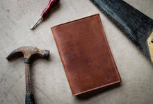 Load image into Gallery viewer, Brown leather notebook with a hammer and chisel on a textured surface
