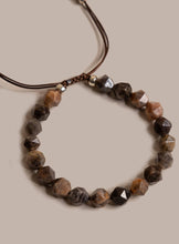 Load image into Gallery viewer, Faceted brown and black gemstone bead necklace on a dark brown cord with silver spacer beads, shown on a solid beige background.