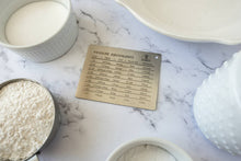 Load image into Gallery viewer, Measurements card on a marble surface with flour, eggs, and a bowl.