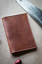 Load image into Gallery viewer, Brown leather wallet on a textured surface with a saw blade in the background