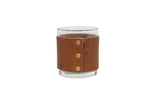 Load image into Gallery viewer, Clear glass tumbler with a brown leather sleeve featuring gold rivets on a white background