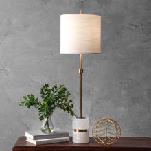 Load image into Gallery viewer, Table lamp with white shade and gold accents on a wooden table against a gray wall.
