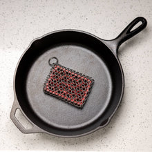 Load image into Gallery viewer, Black cast iron skillet with a red and black scrubber on a light gray surface