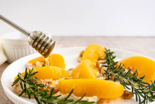 Load image into Gallery viewer, Plate of sliced peaches with honey being drizzled over them on a white background
