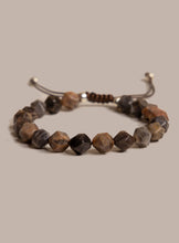 Load image into Gallery viewer, A beaded stretch bracelet made of faceted brown and gray stone beads, with a dark brown cord and metal slider clasp, shown on a solid beige background.