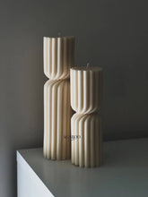 Load image into Gallery viewer, Two beige textured candles on a white surface with a dark background