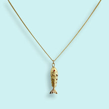 Load image into Gallery viewer, Gold fish-shaped pendant on a chain against a light blue background