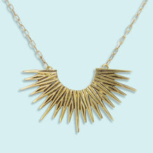 Load image into Gallery viewer, Gold necklace with a sunburst design on a light blue background
