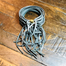 Load image into Gallery viewer, A charcoal deerskin leather cuff bracelet with an antique-brass, magnetic sliding clasp, displayed on a wooden surface.