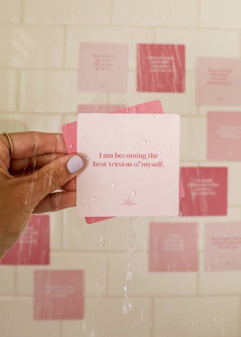 Hand holding a pink card with motivational text against a tiled wall.