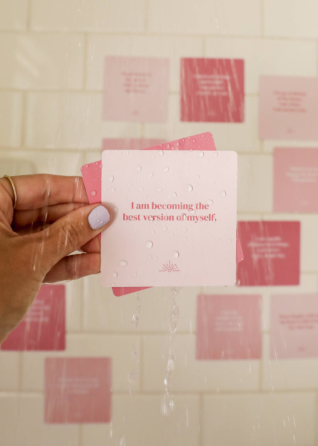 Hand holding a pink card with motivational text against a tiled wall.