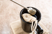 Load image into Gallery viewer, Black mug with a white cloth inside, a silver honey dipper, on a beige background
