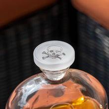Load image into Gallery viewer, Glass bottle with skull and crossbones cap on a dark textured background
