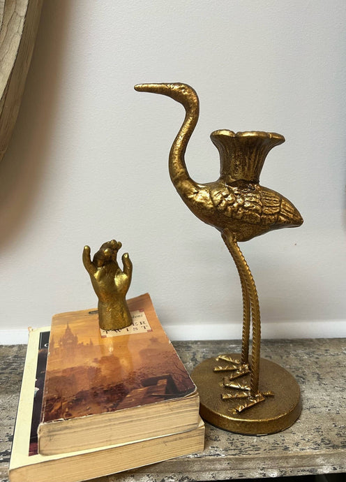 Gold crane candle holder on a wooden surface with a white wall background
