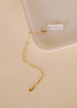 Load image into Gallery viewer, Gold chain necklace on a beige surface with a visible brand tag.

