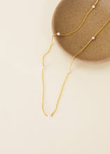 Load image into Gallery viewer, Gold necklace with small pearls on a beige surface
