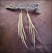 Load image into Gallery viewer, Feather earrings with a decorative metal piece on a brown leather background
