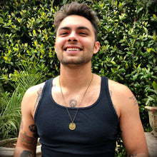 Load image into Gallery viewer, Man wearing a navy tank top with tattoos, standing in front of green foliage.
