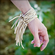 Load image into Gallery viewer, Hand wearing a fringed leather bracelet with a blurred green background
