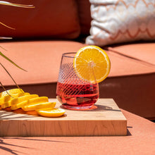 Load image into Gallery viewer, Glass of red cocktail with lemon slices on a wooden board outdoors

