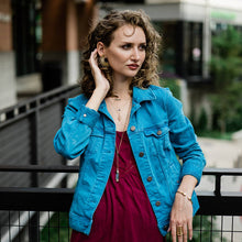 Load image into Gallery viewer, Woman wearing a blue denim jacket over a red dress, standing outdoors.
