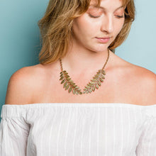 Load image into Gallery viewer, Woman wearing a leaf-shaped necklace against a light blue background
