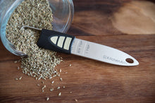 Load image into Gallery viewer, Measuring spoon with KitchenArt logo on a wooden surface with dried herbs.

